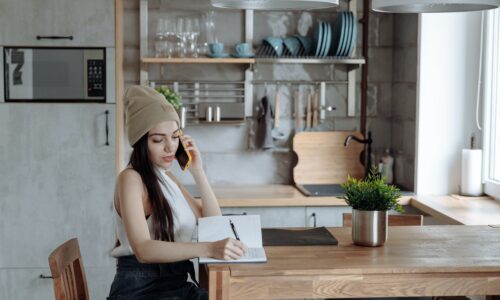 woman on the phone while taking notes in her kitchen